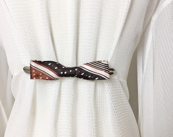 May include: A white shirt with a brown and white patterned bow tie.