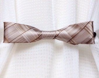 May include: A brown and white patterned bow tie curtain tieback. The tieback is made of a soft, silky fabric and has a simple design.