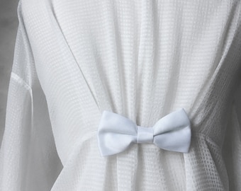 May include: A white robe with a white satin bow tie. The robe is made of a soft, lightweight fabric and has a relaxed fit.