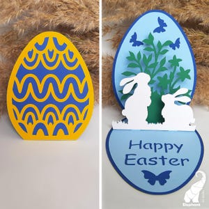 May include: A blue and yellow Easter egg card with a pop-up design. The card features two white bunnies and a green bush with blue butterflies. The card reads "Happy Easter".