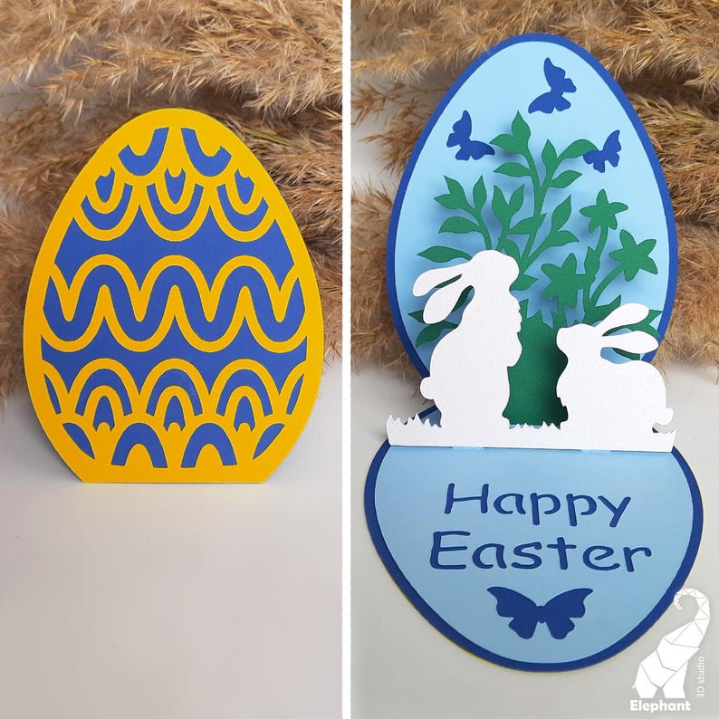May include: A blue and yellow Easter egg card with a pop-up design. The card features two white bunnies and a green bush with blue butterflies. The card reads "Happy Easter".