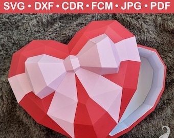 May include: A red and pink heart-shaped box with a bow on top. The box is open and the inside is white. The box is made of paper and is designed to be assembled.