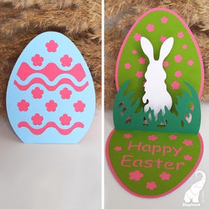 May include: A pop-up Easter card with a blue egg with pink and white designs on the front. The inside of the card has a green egg with a white bunny silhouette and the words "Happy Easter" in pink.