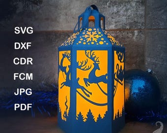Peut inclure: Un modèle de lanterne en papier bleu avec un design festif. La lanterne présente des silhouettes découpées de rennes, d'un traîneau et d'arbres, avec une lueur orange à l'intérieur. Le texte "PAPER LANTERN TEMPLATE" est en haut.