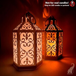 May include: Two decorative lanterns with intricate cut-out designs. The lanterns are lit from within, creating a warm, inviting glow. The text on the image reads "Not for real candles! Only for LED candles or garlands."