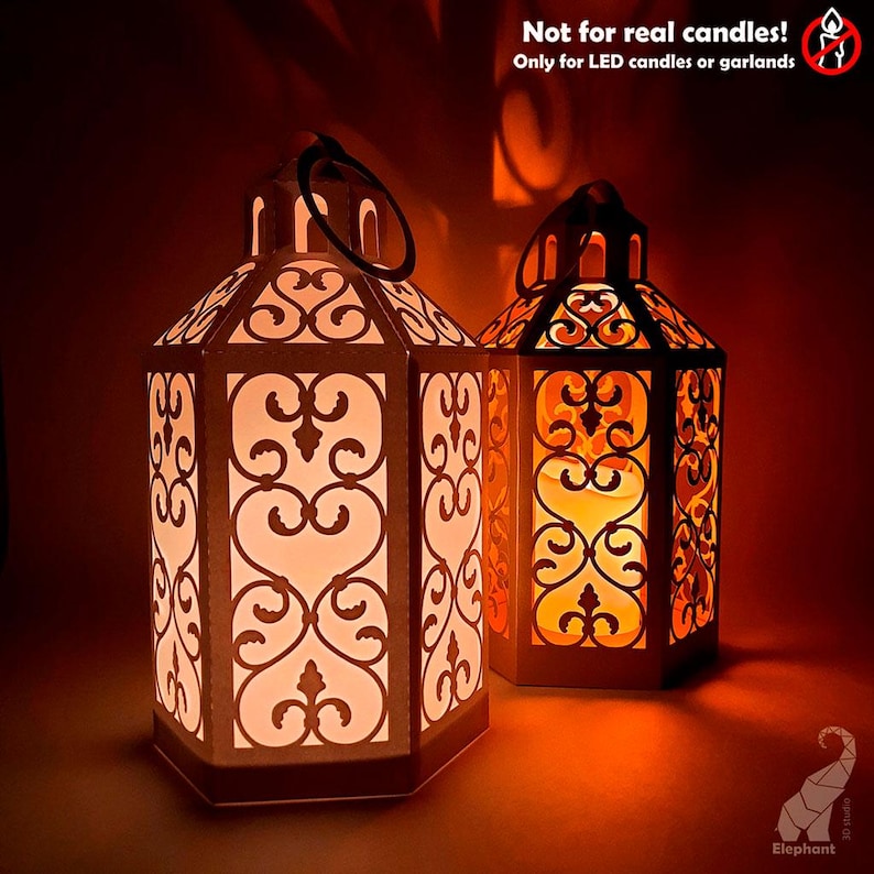 May include: Two decorative lanterns with intricate cut-out designs. The lanterns are lit from within, creating a warm, inviting glow. The text on the image reads "Not for real candles! Only for LED candles or garlands."
