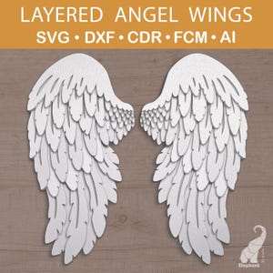 May include: White layered angel wings with a detailed feather design. The image includes the text "LAYERED ANGEL WINGS" and file type options: SVG, DXF, CDR, FCM, and AI. The wings are displayed on a wooden background.