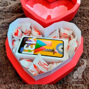 May include: A red heart-shaped box with a white interior. The box is filled with small white wrapped candies and a yellow and white phone box with the text "13M" on it.