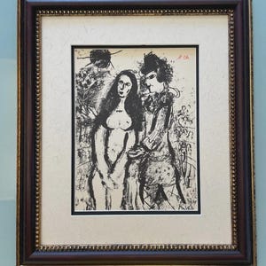 Pode incluir: Impressão a preto e branco de duas figuras, emoldurada numa moldura de madeira castanha escura com acabamento dourado. A obra de arte retrata um homem e uma mulher num estilo estilizado e abstrato. A impressão é montada num passe-partout creme.