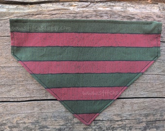 May include: A triangular pet bandana with a green and red striped pattern. The fabric has a textured appearance, and the edges are neatly stitched. The design is reminiscent of a classic horror movie character's sweater.