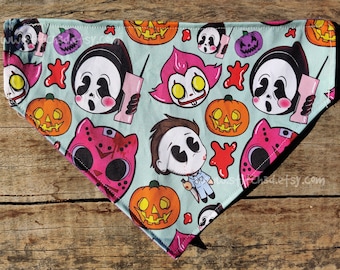 May include: A blue bandana with a Halloween theme featuring cartoon characters from horror movies. The bandana has images of pumpkins, a ghost, a clown, and a masked killer. The bandana is trimmed with black fabric.