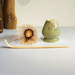 May include: A green ceramic matcha bowl with a floral design, a bamboo matcha whisk, and a bamboo matcha scoop.