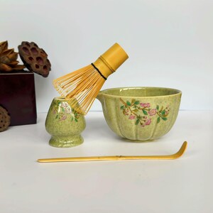 K&ouml;nnte beinhalten: Eine gr&uuml;ne Keramik-Matcha-Schale mit Blumenmuster, ein Bambus-Schneebesen, eine gr&uuml;ne Keramik-Matcha-Tasse mit Blumenmuster und ein Bambus-Matcha-L&ouml;ffel.