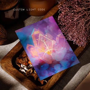 Pode incluir: Uma impressão retangular com um fundo vibrante em tons de roxo, rosa e azul que lembra uma nebulosa, com estruturas cristalinas e um símbolo geométrico central. O texto CUSTOM LIGHT CODE está impresso em branco no topo da imagem.