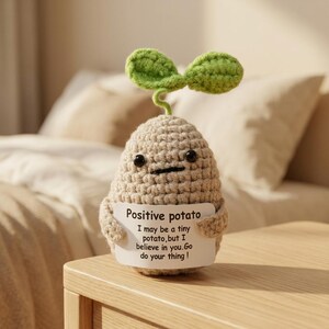Op de afbeelding: Een beige gehaakt aardappelfiguurtje met twee kleine zwarte oogjes en een spruitje met twee groene blaadjes bovenop. Het figuurtje houdt een wit bordje vast met de tekst: Positive potato. I may be a tiny potato, but I believe in you. Go do your thing!