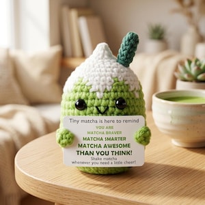 Può includere: Un peluche all'uncinetto verde a forma di bevanda matcha con panna montata bianca e una piccola cannuccia verde. Tiene in mano un cartoncino bianco con il testo: Tiny matcha is here to remind YOU ARE MATCHA BRAVER MATCHA SMARTER MATCHA AWESOME THAN YOU THINK!