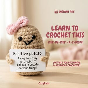 Könnte beinhalten: Eine beige gehäkelte Kartoffelfigur mit rosa Schleife, schwarzen Perlenaugen und gesticktem Lächeln, die ein weißes Schild mit der Aufschrift Positive potato I may be a tiny potato, but I believe in you. Go do your thing! hält. Text: LEARN TO CROCHET THIS.