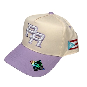 May include: A cream-colored baseball cap with a lavender brim. The cap features the letters "PR" in white, a Puerto Rican flag patch, and a "Hat Vendor" sticker.