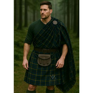 May include: A person wearing a traditional Scottish kilt outfit. The outfit includes a green v-neck shirt, a tartan kilt with green and yellow plaid, a matching plaid shawl, a brown leather belt, and a sporran. A silver brooch secures the shawl.
