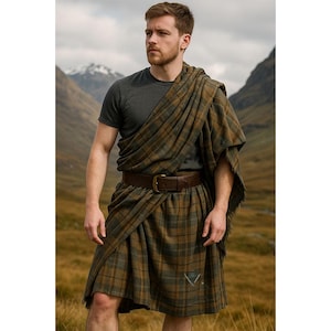 May include: A man wearing a traditional Scottish kilt outfit. The kilt is a brown and green plaid pattern, paired with a brown leather belt and a matching plaid shawl. The outfit includes a gray t-shirt.