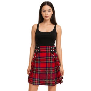 May include: A red plaid kilt with black leather straps and silver-tone hardware. The kilt features a traditional tartan pattern with yellow and navy blue accents. The model is wearing a black tank top.