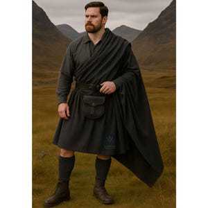 May include: A man in a dark gray kilt outfit, including a long-sleeved shirt, kilt, and a draped shawl. The outfit features a black belt with a pouch, dark socks, and boots. The background shows a grassy field and mountains.