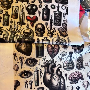 May include: Fabric with a repeating pattern of anatomical and gothic illustrations. Skulls, hearts, brains, eyes, and potion bottles are depicted in black and white with red accents. The fabric has a cream-colored background.