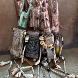 May include: A group of handcrafted rabbit figures with elongated ears and painted faces. The figures are made from paper and wood, with one holding a sign for the "Black Rabbit Tavern". Wooden beads spell out the name "JACK".