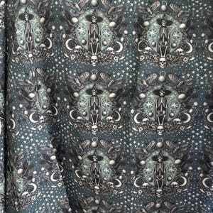 May include: Dark teal fabric with a repeating pattern of skeleton figures wearing witch hats, surrounded by moons, stars, skulls, and wings. The design has a gothic or occult theme, with a celestial and mystical aesthetic.