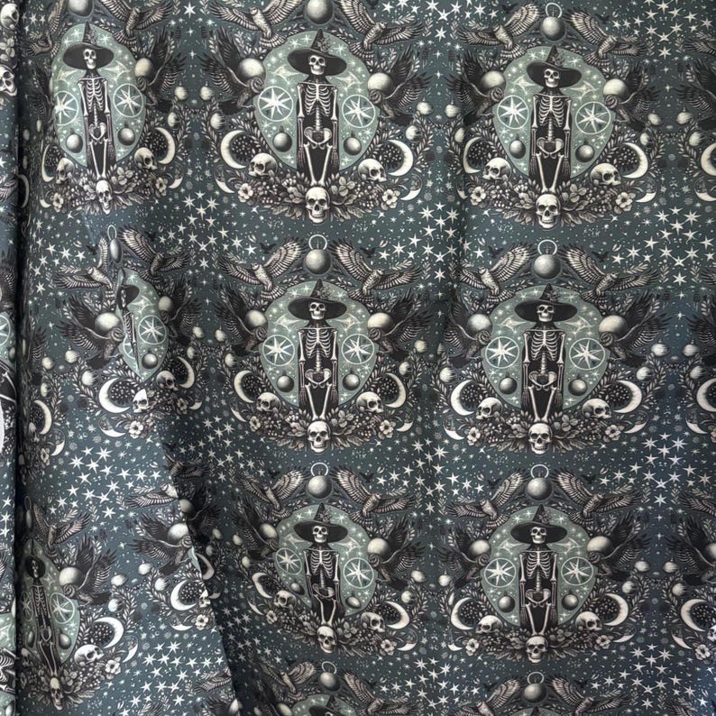 May include: Dark teal fabric with a repeating pattern of skeleton figures wearing witch hats, surrounded by moons, stars, skulls, and wings. The design has a gothic or occult theme, with a celestial and mystical aesthetic.