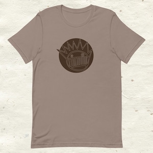 May include: A brown t-shirt with a brown outline of a cartoon face with a crown of spikes and a mouth with teeth.