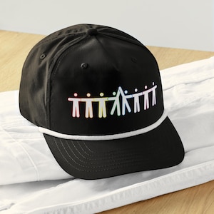 May include: Black baseball cap with a white rope detail and a rainbow graphic of stick figures holding hands. The cap has a curved brim and a structured crown.