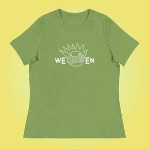 Puede incluir: Una camiseta verde para mujer con un gráfico blanco de una cara de dibujos animados con el texto "WE EN" debajo.