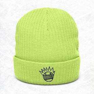 May include: A neon green beanie with a ribbed knit texture. The beanie features a black graphic of a crown with a face on the front. This winter hat is a stylish accessory.