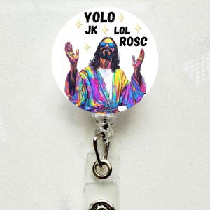 May include: A white badge reel with a colorful illustration of a figure with sunglasses and long hair, arms raised. The text "YOLO JK LOL ROSC" is printed above the figure. The reel has a silver clip and a clear plastic holder.