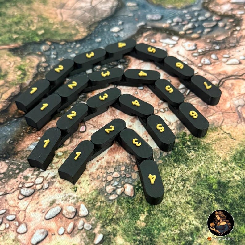 May include: Black, rectangular game pieces with gold numbers from 1 to 7. The pieces are arranged in a pattern on a textured surface. The game pieces are likely for a board game or tabletop game.