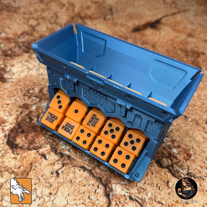 May include: A blue dice box with orange dice. The box is rectangular with a hinged lid and a compartment to hold the dice. The orange dice have black dots and the text "TYCKA DICE".