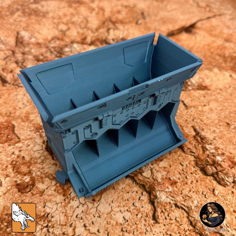 May include: A teal-colored, rectangular container with a series of internal dividers. The container has a detailed, industrial design with rivets and paneling. The object is likely a storage solution or organizer.
