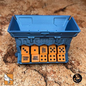 May include: A blue dice storage container with orange dice. The container has a rectangular shape with a slot for each die. Each die has black dots and the text "TYCKA DICE".