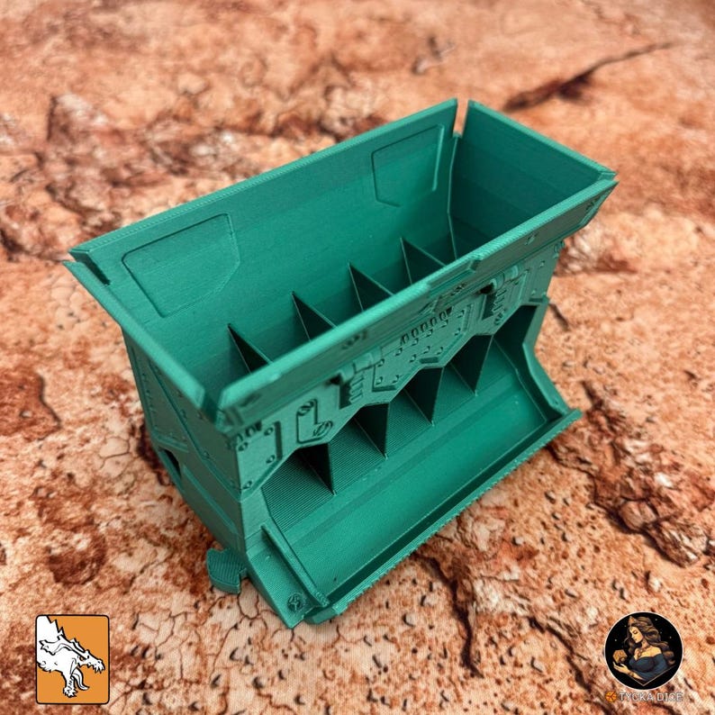 May include: A teal-colored, rectangular container with a series of internal dividers. The container has a detailed, textured surface with what appears to be a mechanical or industrial design. The object is likely a storage or organizational unit.