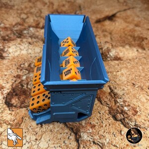 May include: A blue dice storage container filled with orange dice. The dice have black dots and the text "TYCKA DICE". The container is made of a rigid material and has a textured surface.