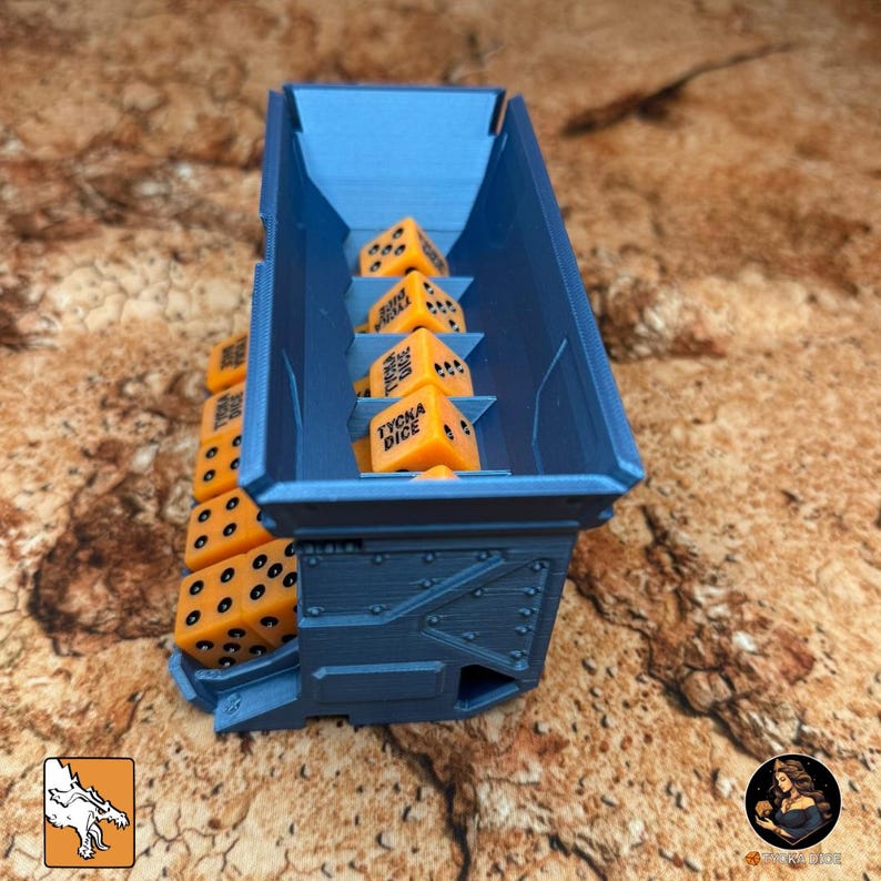 May include: A blue dice storage container filled with orange dice. The dice have black dots and the text "TYCKA DICE". The container is made of a rigid material and has a textured surface.