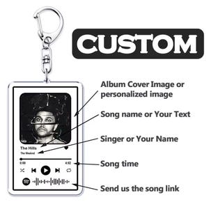 Puede incluir: Un llavero rectangular con un cierre plateado. El llavero presenta una imagen en blanco y negro de un músico, detalles de la canción y la palabra "CUSTOM". El diseño incluye una interfaz de reproductor de música con información de la canción.