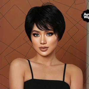 May include: A woman with dark hair wearing a black top. The woman is wearing a short, black wig. The background is a brown color with a geometric pattern. The Aura Wigs logo is in the top right corner.