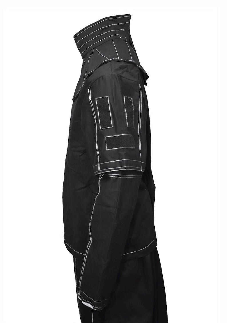 May include: A black jacket with white stitching detail. The jacket has a high collar and a zipper closure. The jacket has two pockets on the front and two pockets on the inside. The jacket is made of a lightweight fabric and is perfect for layering.