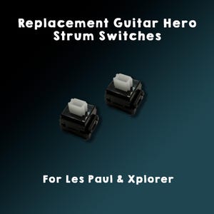 May include: Two black replacement Guitar Hero strum switches with white tops. The text "Replacement Guitar Hero Strum Switches" is at the top of the image. The text "For Les Paul & Xplorer" is at the bottom of the image.