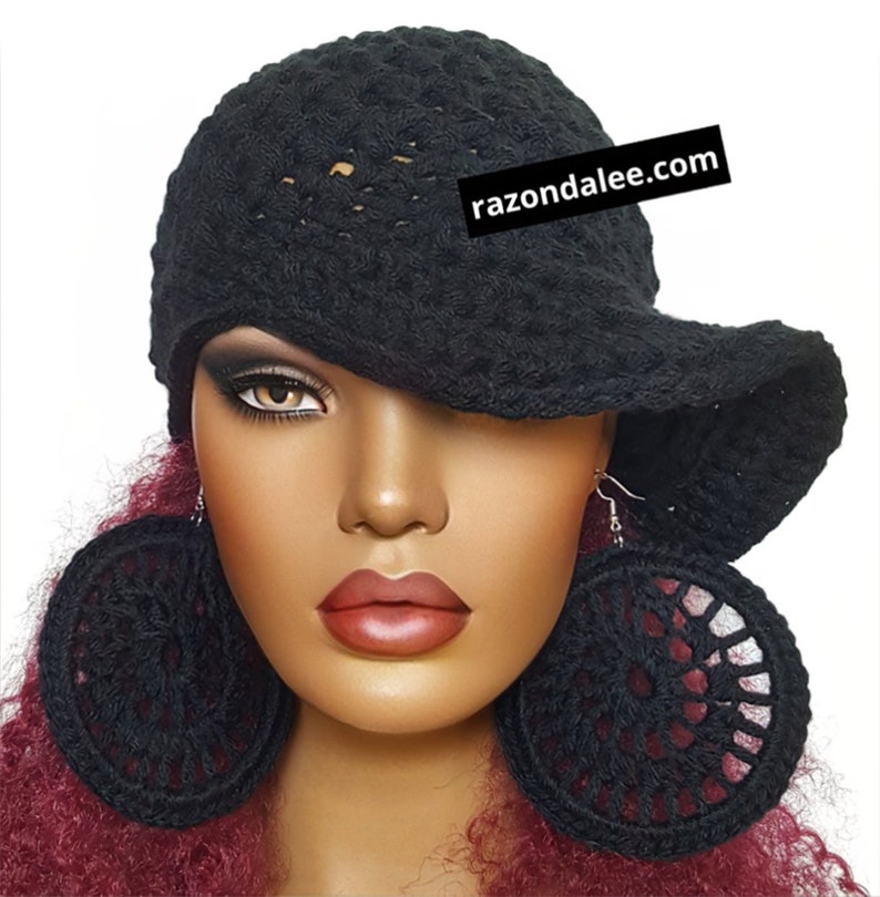 May include: A black crocheted hat with a wide, asymmetrical brim and a pair of large, circular black crocheted earrings. The hat features the text razondalee.com printed on a black rectangular label attached to the side of the crown.