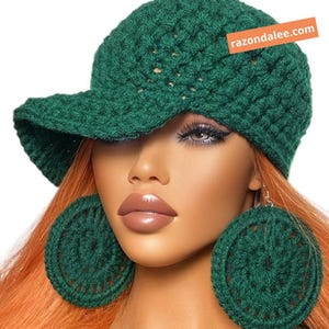 May include: A dark green crocheted baseball cap with a textured stitch pattern and a matching pair of large, circular crocheted earrings. The cap features an orange rectangular tag with the white text razondalee.com.