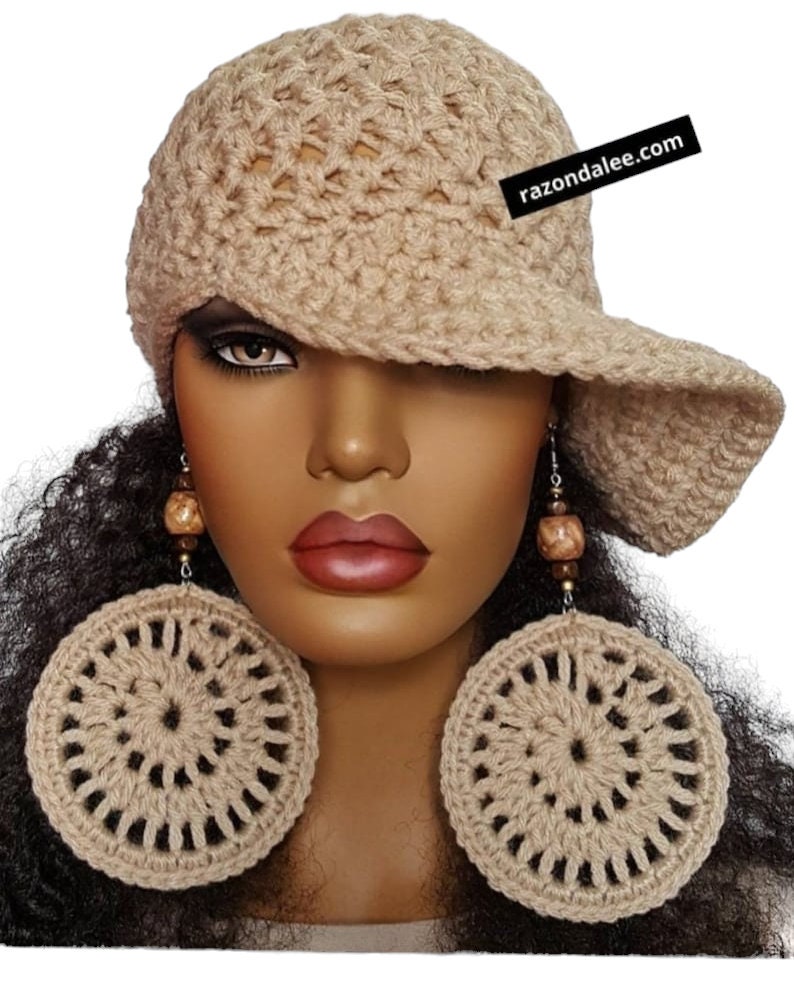 May include: A beige crochet hat with a wide brim and a black tag reading razondalee.com, paired with large, circular beige crochet earrings featuring brown wooden beads on silver-toned metal hooks.