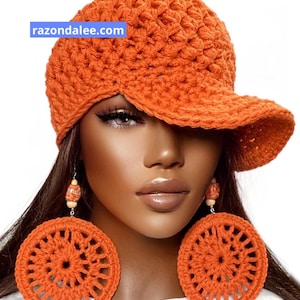 May include: An orange crocheted baseball cap with a textured knit pattern and the text razondalee.com. Large, round, orange crocheted earrings with a circular openwork design and small wooden beads hang from the ears.